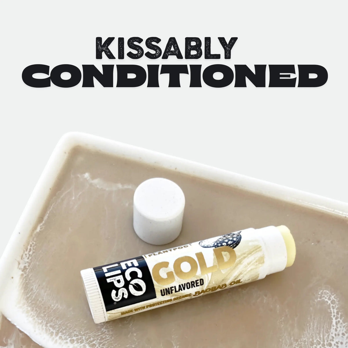 Lip balm tube labeled 'Gold Unflavored' by Eco Lips on a beige plate with 'Kissably Conditioned' text above.