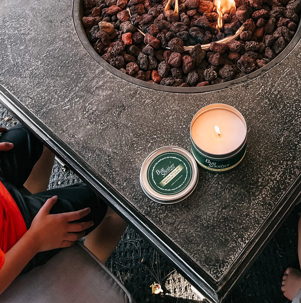 A Bug Soother candle lit on a firepit table. 